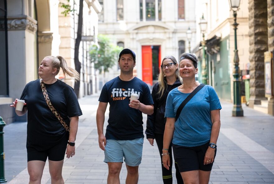 Three people on a walking tour with a Fit City tour guide, two carrying a takeaway coffee.