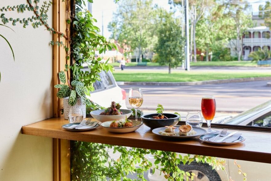 A window seat at a leafy restaurant with a variety of dishes and drinks.