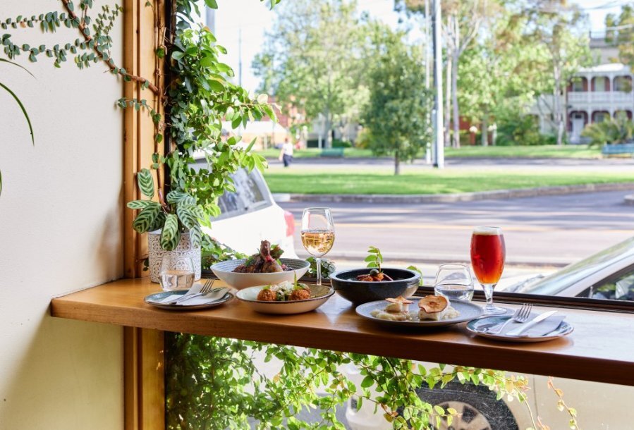 A window seat at a leafy restaurant with a variety of dishes and drinks.