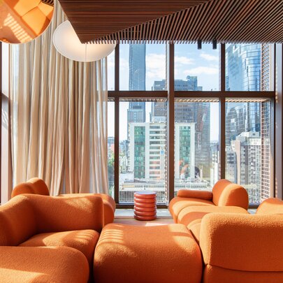 An orange modular sofa in a room with floor to ceiling windows and a city view. 