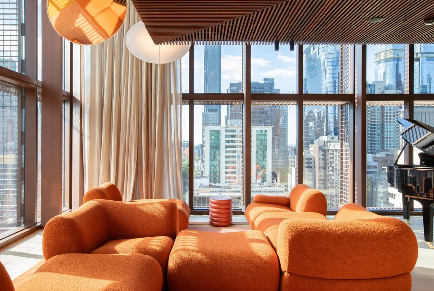 An orange modular sofa in a room with floor to ceiling windows and a city view. 