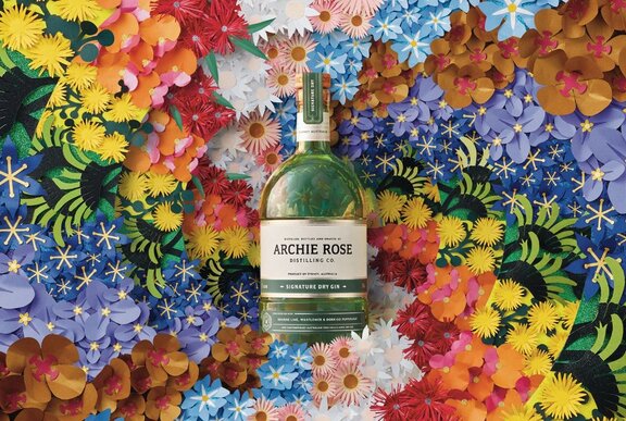 A bottle of Archie Rose signature dry gin resting on a bed on colourful paper flowers.