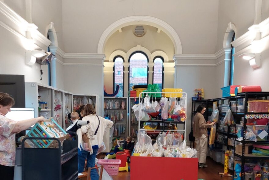 The toy library at Carlton, housed in a large room filled with shelves and racks of toys with parents browsing.