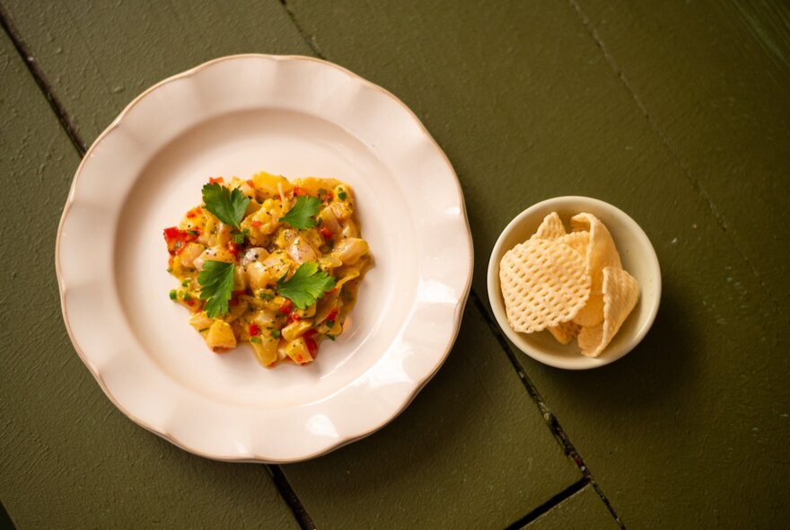 Looking down on a small plate with a garnished snack and lattice chips in a side bowl. 