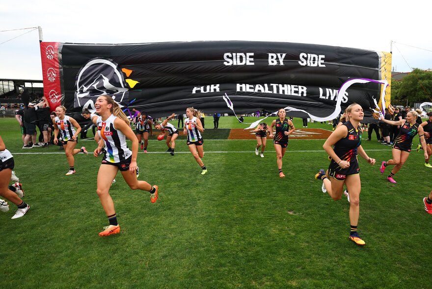 The Collingwood Magpies AFLW team running through the banner before the game.
