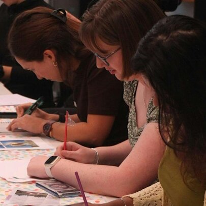 People seated at a table working on creative projects with pencils and paper.
