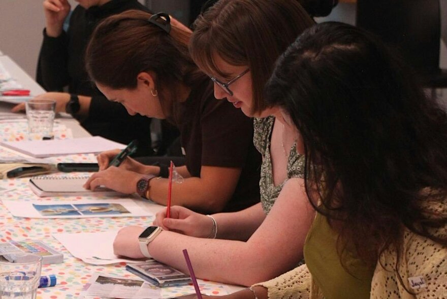 People seated at a table working on creative projects with pencils and paper.