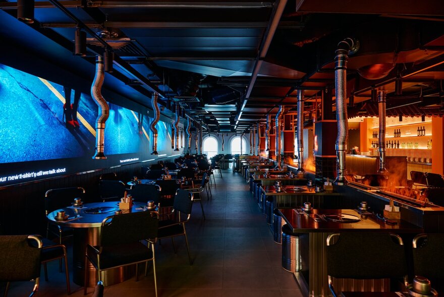 Dimly lit dining area with long line of tables and atmospheric blue lighting.