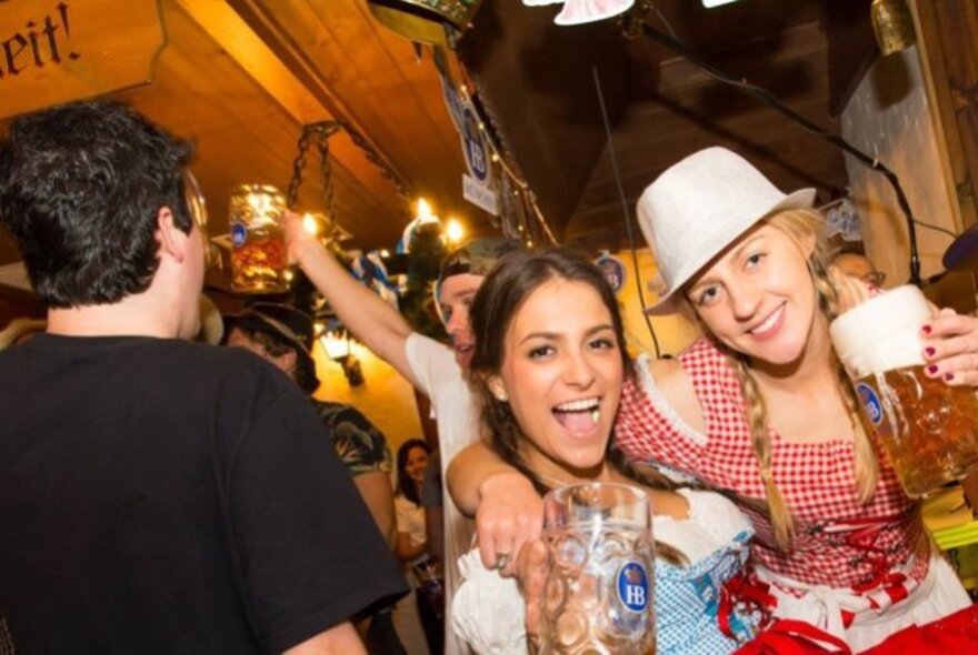 Two girls laughing with large beer jugs in a pub atmosphere.