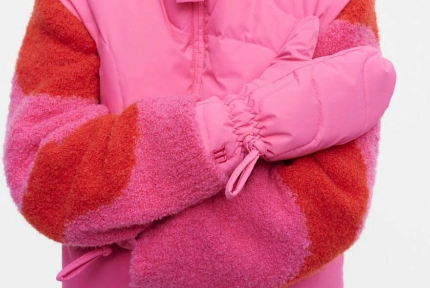 A person is wearing a pink outfit and pink mittens 