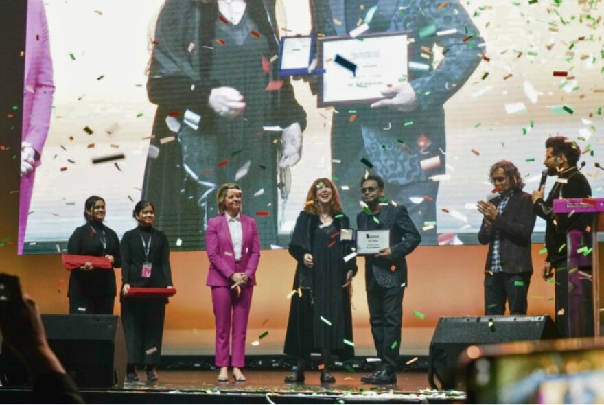 People on a stage receiving awards at the Indian Film Festival awards night, with confetti raining down on them.