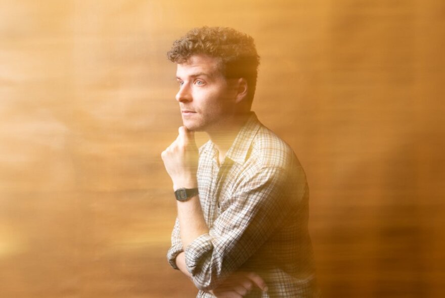 A sepia-washed images of Oliver Coleman, thinking with his hand on his chin. 