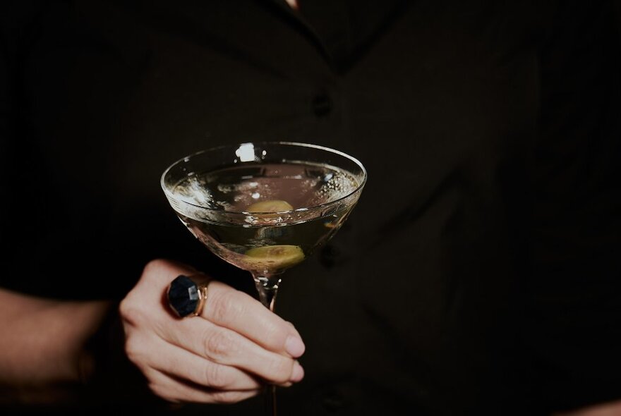 A hand holding a martini cocktail in a glass.