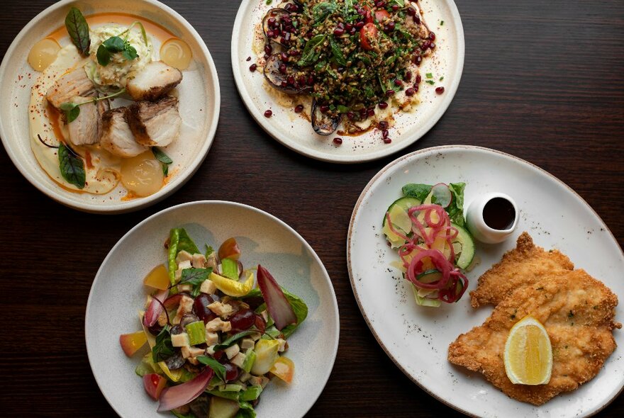 Overhead view of meals served on white plates on a dark table surface.