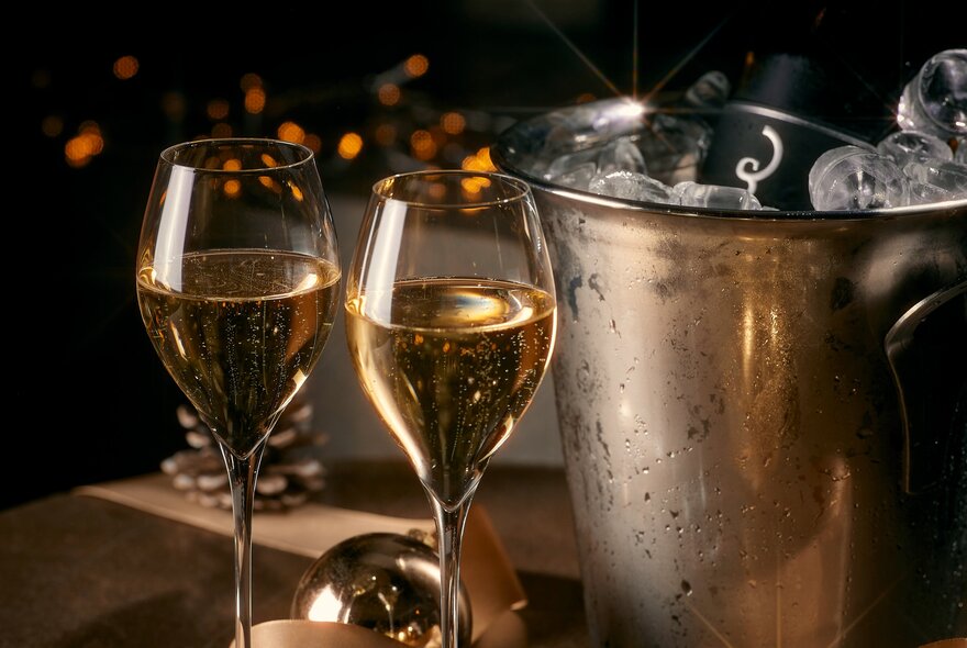 Two glasses of sparkling wine next to an ice bucket.