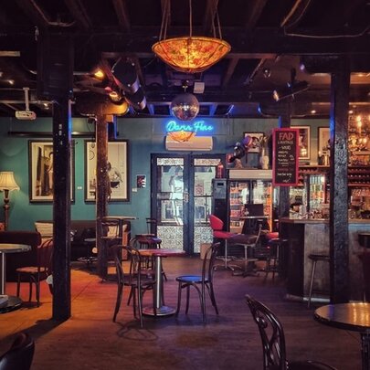 Interior of Fad Gallery Bar with small tables and chairs, a bar area, artwork on the walls and table lamps.