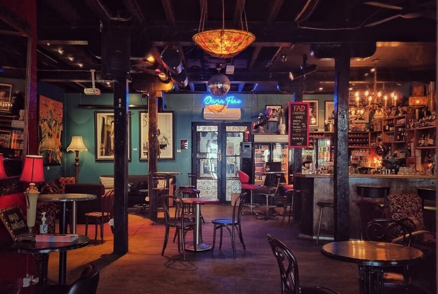 Interior of Fad Gallery Bar with small tables and chairs, a bar area, artwork on the walls and table lamps.
