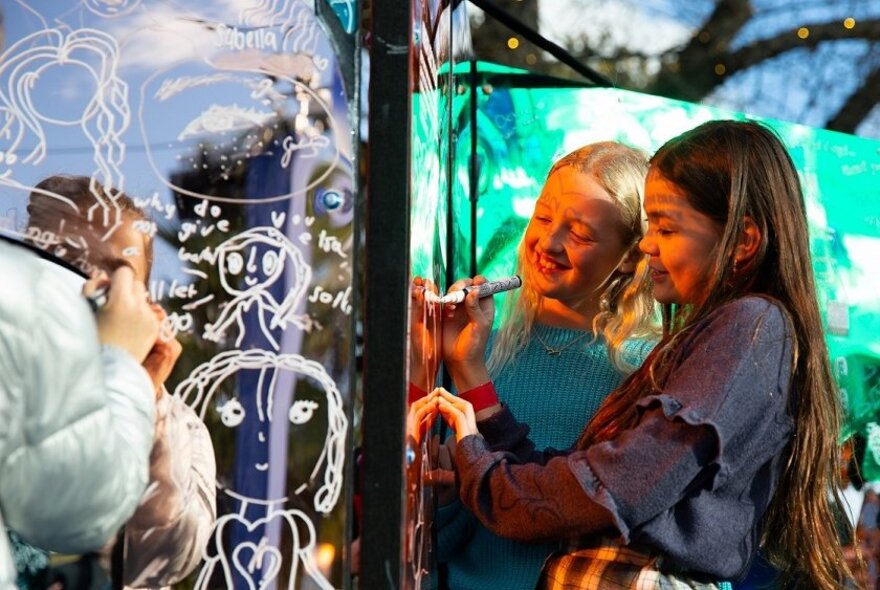 Two teenagers writing messages on a reflective scribble wall at the RESET Festival at Fed Square.