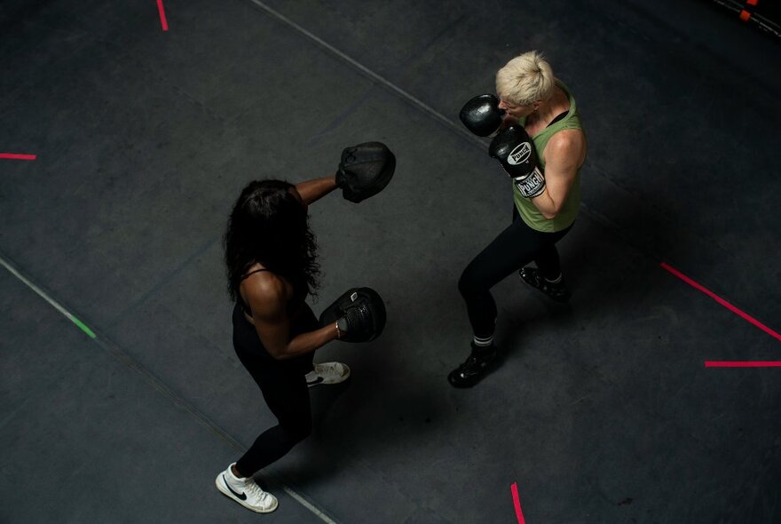 Aerial view of two people wearing black boxing gloves and sparring inside a boxing ring.