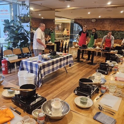 Cooking class tables and participants in a restaurant setting with portable stoves and ingredients.