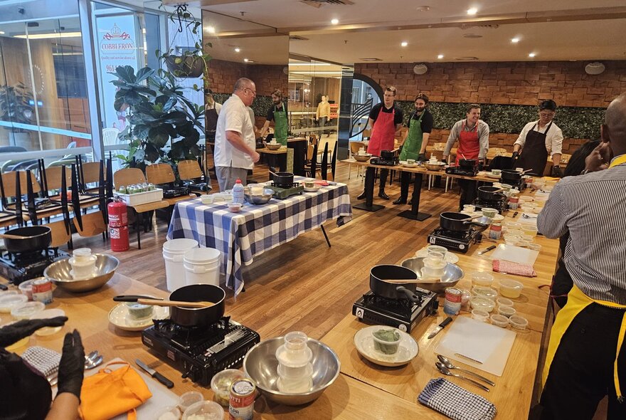 Cooking class tables and participants in a restaurant setting with portable stoves and ingredients.