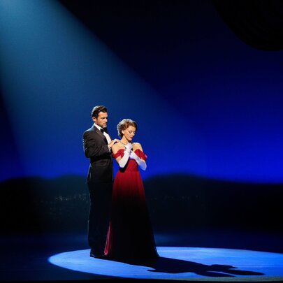 Two actors wearing formal clothes in a spotlight on a theatre stage during a performance of Pretty Woman: The Musical.