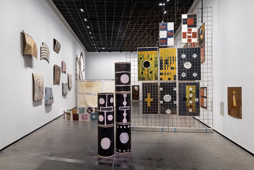 An exhibition space at a gallery with Indigenous artworks presented on the walls and a wire screen.