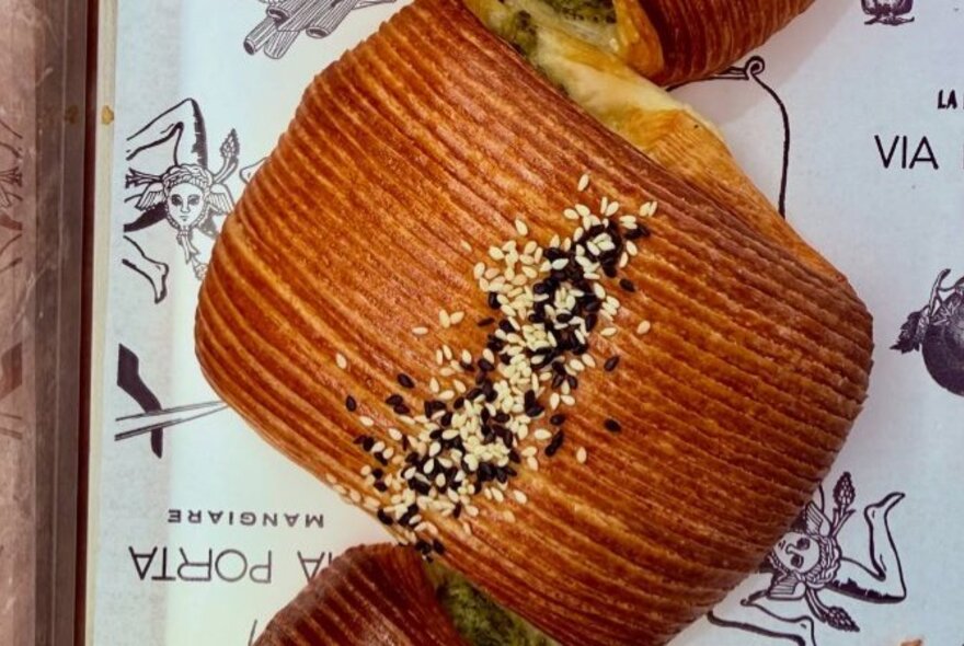A silverbeet, kale and feta croissant on a tray with a paper liner covered in printed drawings.