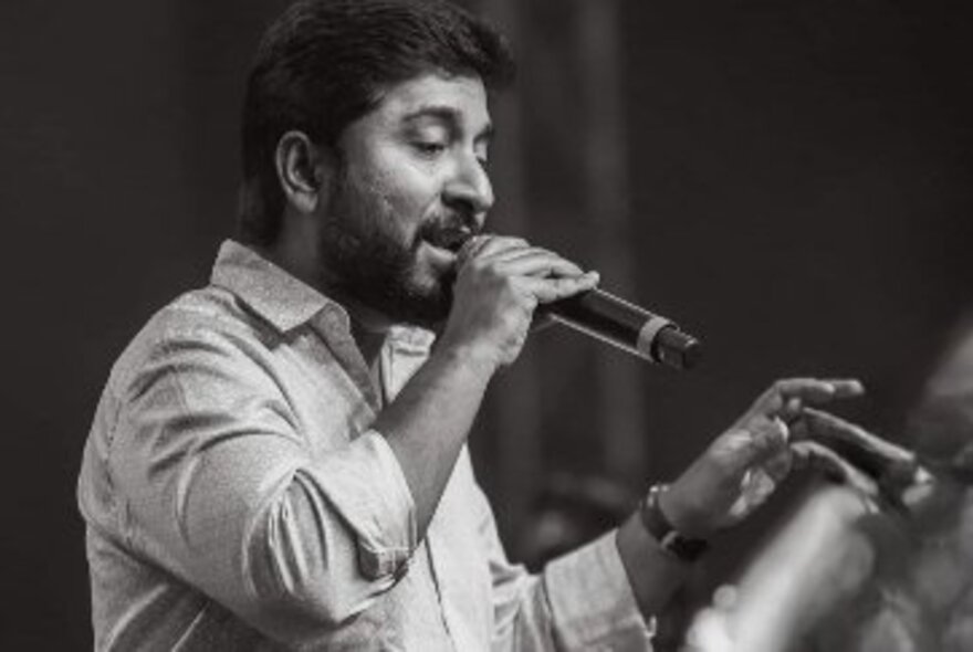 Actor and musician Vineeth Sreenivasan, a man aged about 40 years, singing into a microphone the holds in his hand, in profile view.