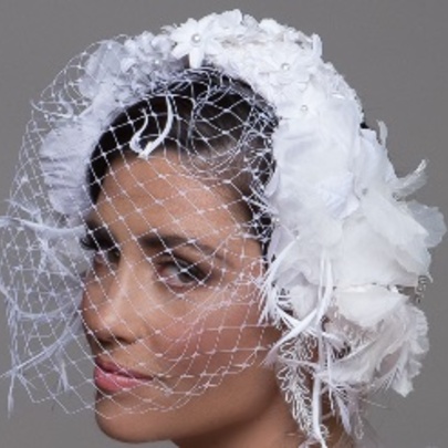 Model wearing a white feather fascinator with veil against a grey background.