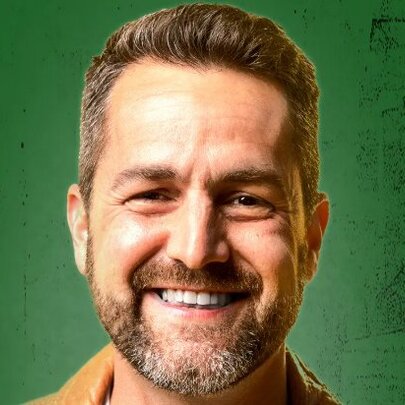 Close-up of the smiling face of comedian Ivan Aristeguieta, against a green background.