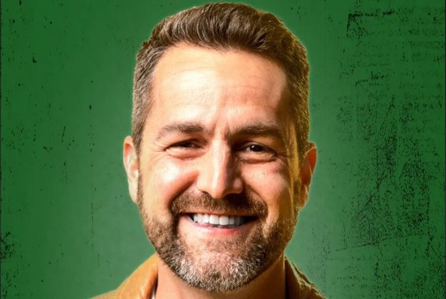 Close-up of the smiling face of comedian Ivan Aristeguieta, against a green background.