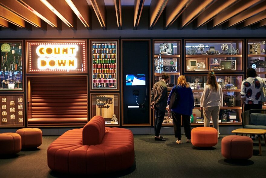 People looking at a museum display of Countdown memorabilia, large cushioned seats scattered around the area. 