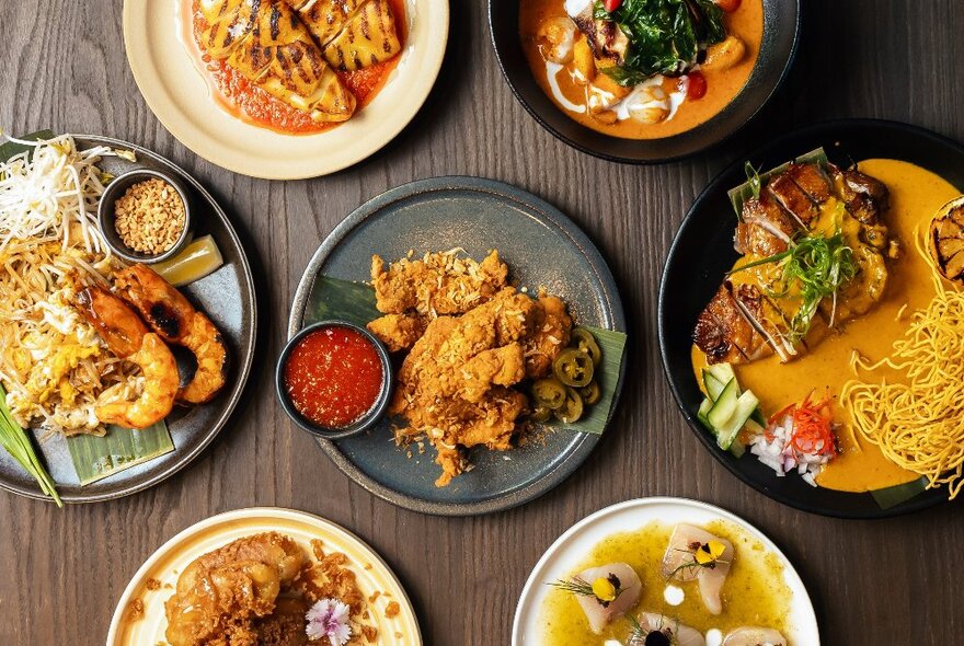 An array of delicious-looking traditional Thai dishes displayed on a wooden table, seen from above.