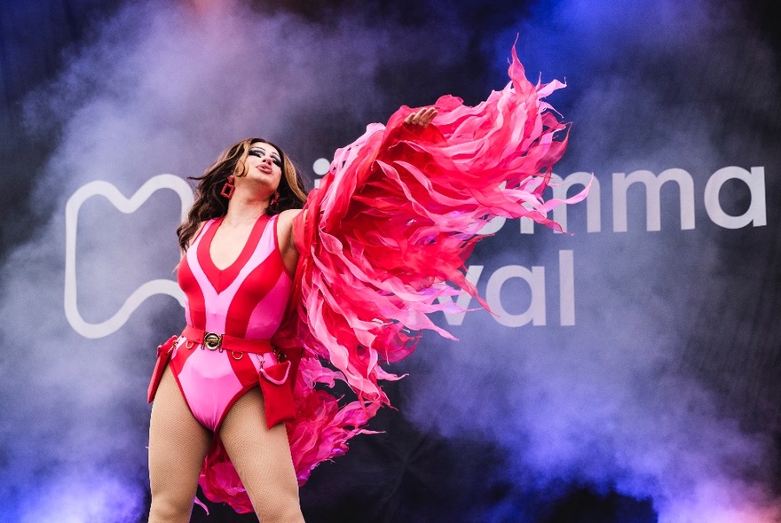 A drag queen on stage, dressed in a feathery pink and red outfit.