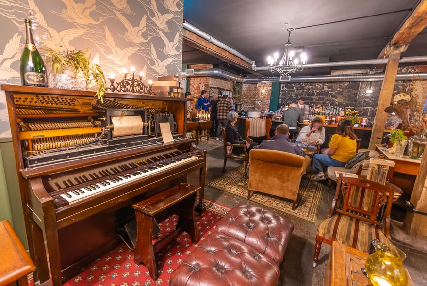 A group of friends are drinking cocktails in a basement bar with an old piano