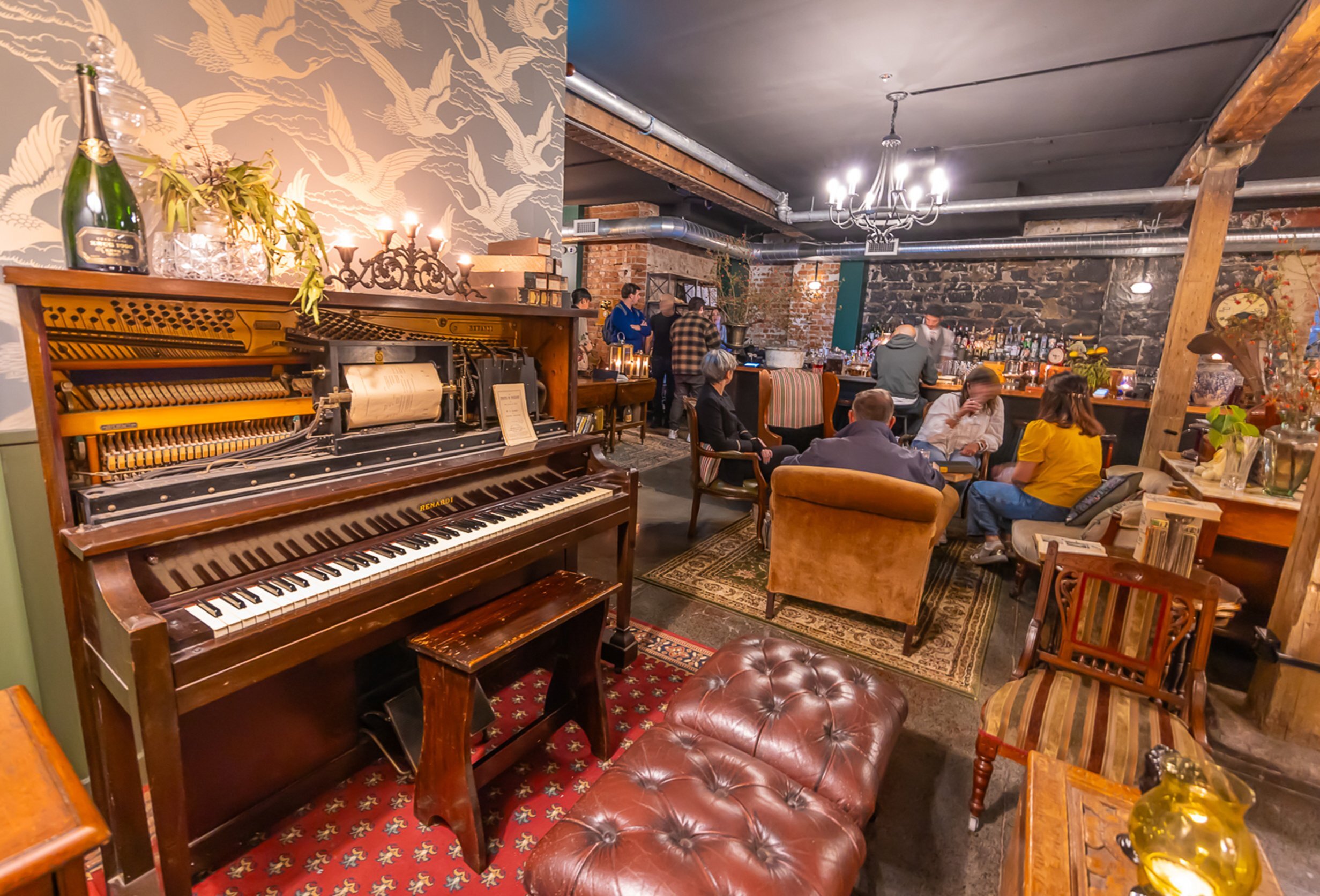 A group of friends are drinking cocktails in a basement bar with an old piano