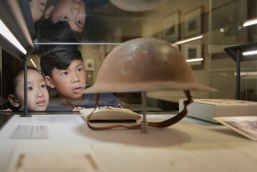 Two young children looking at a metal soldier's helmet in a glass display case at the Shrine.
