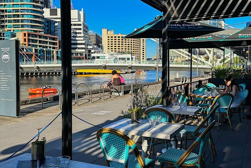 An empty riverside dining area with aqua chairs on a sunny day