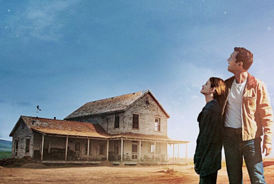 A still from the film, Interstellar, showing a father and daughter looking up at a blue sky in front of their dilapidated farmhouse.