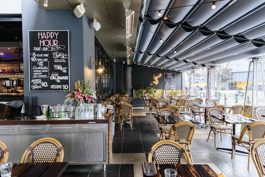 The interior of Breslin Steakhouse with tables and rattan dining chairs, and a central bar area.