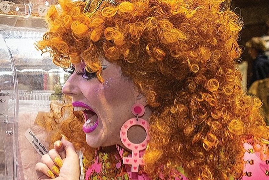 Drag performer wearing a curly orange wig, screaming.
