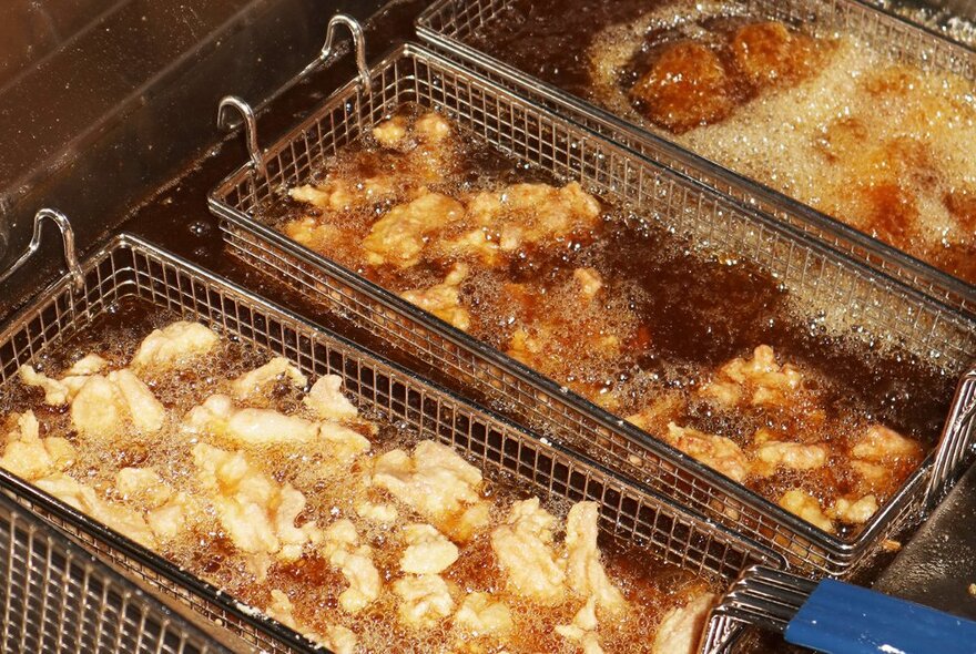 Three fryer baskets in the fryer with Japanese karaage chicken frying.