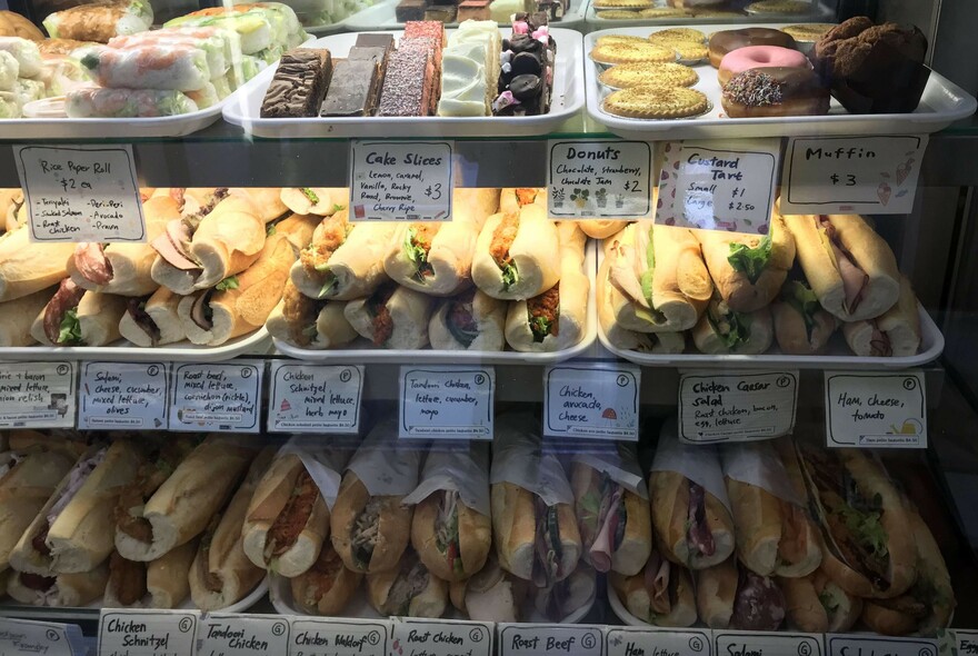 Counter falloff three trays of pastries and baguette sandwiches.