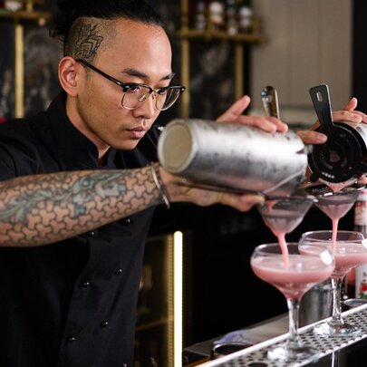 A bartender carefully pouring two pink cocktails.