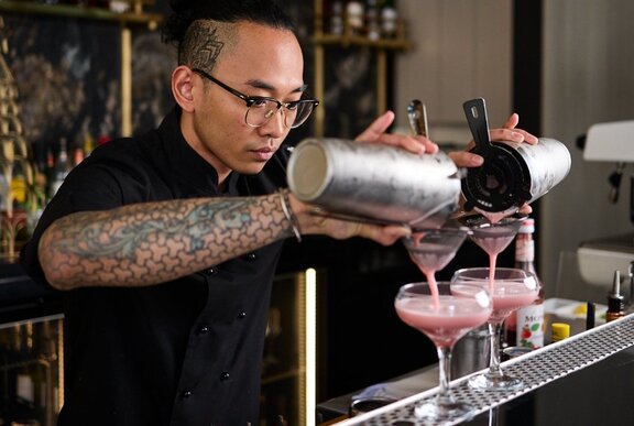 A bartender carefully pouring two pink cocktails.