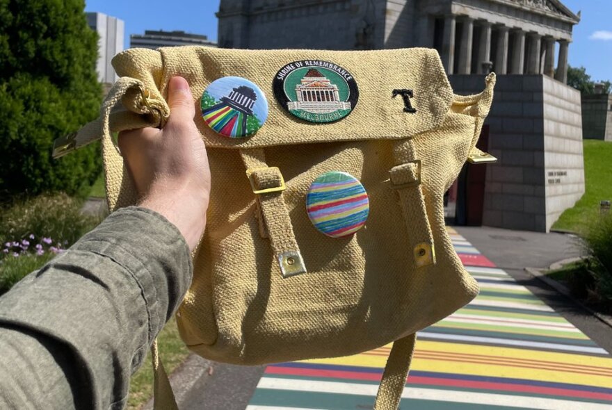 A hand holding a hessian kit bag with medals inspired by the Shrine.