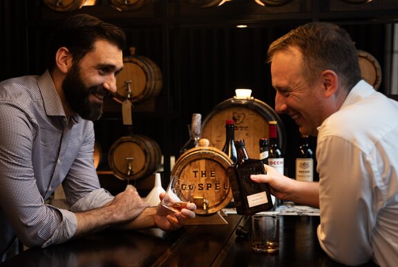Two renowned bartenders either side of a bar table, leaning over, smiling and laughing.