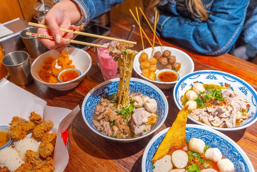 Person holding noodles above bowl on crowded table