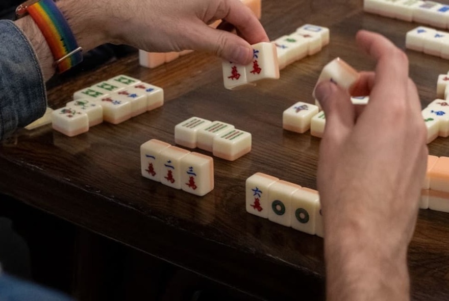 Hands arranging mahjong tiles on a table during a game.